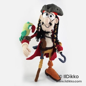 May include: A crocheted pirate doll with a dark gray hat, black hair, and a mustache. The doll wears a red coat, tan pants, and brown boots, with a hook hand and a small green parrot perched on the other arm. Text reads: © Ildikko www.ildikko.com