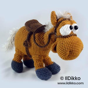 May include: A crocheted horse toy in golden brown yarn with dark gray hooves, a white mane and tail, and a dark brown saddle. The horse features large white eyes with black pupils, a dark brown bridle, and the text "© Ildikko www.ildikko.com".