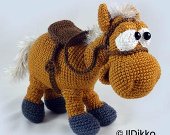 May include: A crocheted horse toy in golden brown yarn with dark gray hooves, a white mane and tail, and a dark brown saddle. The horse features large white eyes with black pupils, a dark brown bridle, and the text "© Ildikko www.ildikko.com".