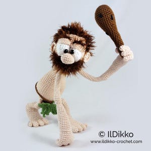 May include: A crocheted caveman doll with beige skin, a brown fuzzy beard, and a green leaf-like loincloth. The figure is in a hunched pose, holding a brown crocheted club overhead. Text at the bottom reads &copy; ILDikko www.ildikko-crochet.com.