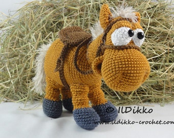 May include: A crocheted brown horse with a saddle, white eyes, and black pupils. The horse has a white mane and tail and is standing on a hay bale. The horse is wearing blue booties.