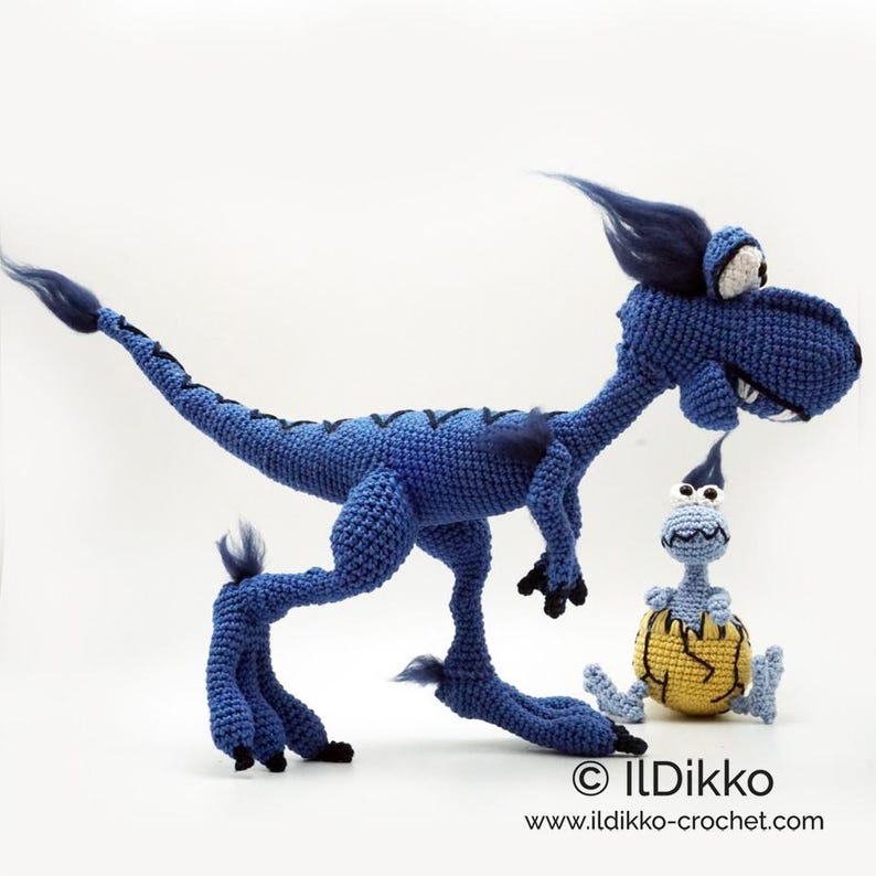 May include: A large blue crocheted dinosaur with a long tail, dark blue tufts, and white eyes, standing next to a smaller light blue crocheted creature emerging from a yellow cracked egg. Text reads: &copy; IlDikko www.ildikko-crochet.com