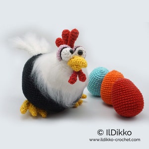 May include: A crocheted black and white chicken with a red comb and yellow beak, holding three crocheted eggs in blue, orange, and red.