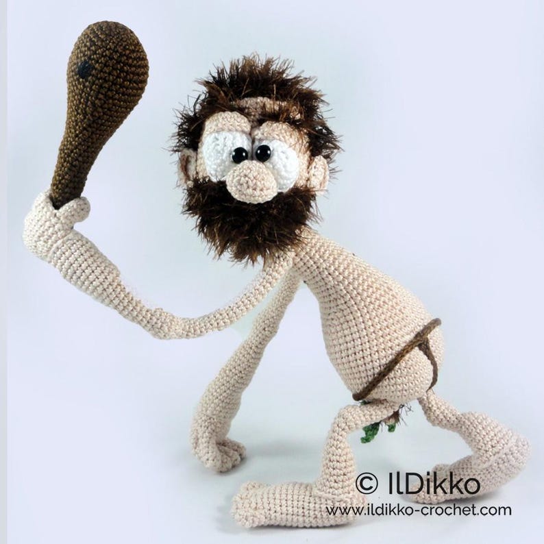 May include: A crocheted caveman doll with beige skin, a dark brown fuzzy beard, and large white eyes with black pupils. The figure holds a brown club in one hand and wears a brown loincloth. Text at the bottom reads: &copy; ILDikko www.ildikko-crochet.com