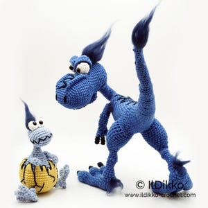 May include: A large blue crocheted dinosaur with dark blue tufts of hair and a smaller light blue crocheted dinosaur emerging from a yellow cracked egg. Both figures have large white eyes with black pupils. Text reads: &copy; Ildikko www.ildikko-crochet.com