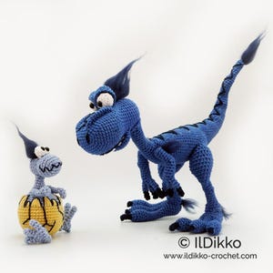 May include: A blue crocheted dinosaur with black claws and a tuft of dark hair, standing next to a smaller light blue crocheted creature emerging from a yellow cracked egg. The text ILDikko and www.ildikko-crochet.com appears at the bottom.