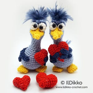 May include: Two blue crocheted birds holding red crocheted hearts. Three smaller red crocheted hearts are in the foreground. The text "© IlDikko www.ildikko-crochet.com" is in the lower right corner of the image.