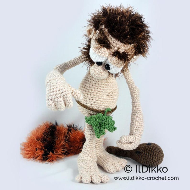 May include: A crocheted caveman doll with beige skin, messy brown hair, and a green leaf loincloth. The figure has large eyes, a brown club, and a separate fuzzy orange and black textured piece. Text reads: ILDikko www.ildikko-crochet.com