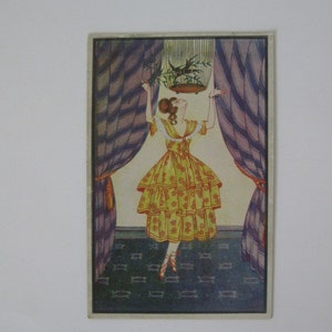 May include: A woman in a yellow dress with red floral accents stands in a room with purple and white striped curtains. She is looking up at a birdcage hanging from the ceiling. The birdcage is filled with green plants and a bird.