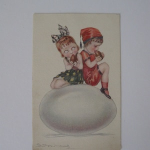 May include: Two children, one wearing a red hat and the other with a black and white bow, sit on a large white egg. They are both holding brown eggs in their hands.