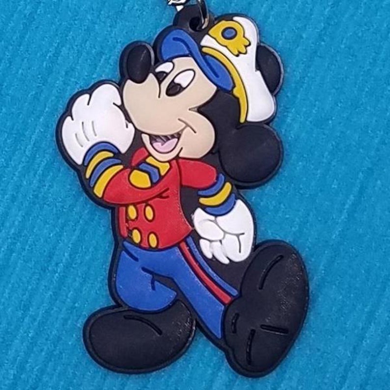 May include: A cartoon Mickey Mouse figurine wearing a blue sailor hat and red and blue uniform. The figurine is made of rubber and has a black and white color scheme.