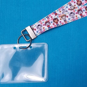 Puede incluir: Un porta credenciales de plástico transparente con un anillo de metal plateado y una cinta blanca con personajes de dibujos animados coloridos.