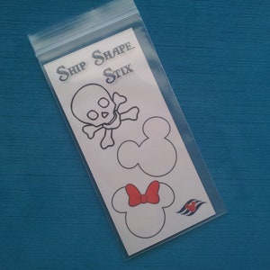 May include: A white sheet of paper with the text "Ship Shape Stix" printed at the top. The paper contains three black and white outlines of a skull and crossbones, a Mickey Mouse head, and a Minnie Mouse head with a red bow. The bottom right corner of the paper has a blue and white Disney Cruise Line logo.