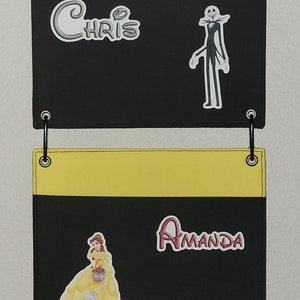 May include: A black fabric wall organizer with four pockets, each with a different colored top: black, white, yellow, and lavender. The organizer features Disney-themed stickers and names: Chris, Jack Skellington, Amanda, Belle, Teresa, and Elsa.