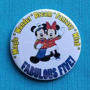 Pode incluir: Um botão branco com uma imagem colorida do Mickey Mouse e da Minnie Mouse vestidos de capitães. O texto ao redor da imagem diz "Magic * Wonder * Dream * Fantasy * Wish * Fabulous Five!"