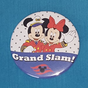 May include: A round button with a white background featuring Mickey Mouse and Minnie Mouse dressed as captains. The text "Grand Slam!" is written in blue on a blue background with a Disney Cruise Line logo.