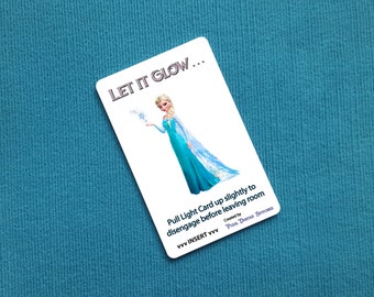Puede incluir: Una tarjeta blanca con una ilustración azul y blanca de una princesa sosteniendo un copo de nieve. El texto en la tarjeta dice "LET IT GLOW... Pull Light Card up slightly to disengage before leaving room Created by vvv INSERT vvv Pox. Der Sc"