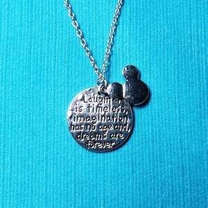May include: Silver-toned necklace with a pendant featuring the quote "Laughter is timeless, imagination has no age and dreams are forever." Includes a small Mickey Mouse head charm. The chain is delicate, and the background is a solid teal color.