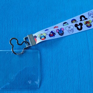 May include: A white lanyard with a Mickey Mouse head design and a clear plastic ID badge holder. The lanyard has a silver metal clasp and a Mickey Mouse head shaped ring.