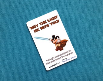 May include: A white card with a cartoon image of Mickey Mouse holding a lightsaber. The card reads "May the Light Be With You!" and includes instructions to pull the card up slightly to disengage before leaving the room. The card is created by Pozz Duster Services.