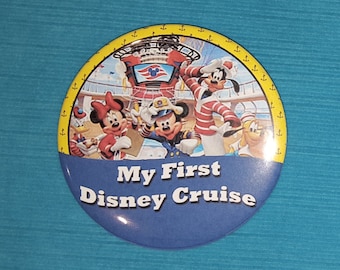 May include: A blue and yellow round button with the text "My First Disney Cruise" and images of Mickey Mouse, Minnie Mouse, Goofy, and Donald Duck in front of a cruise ship.