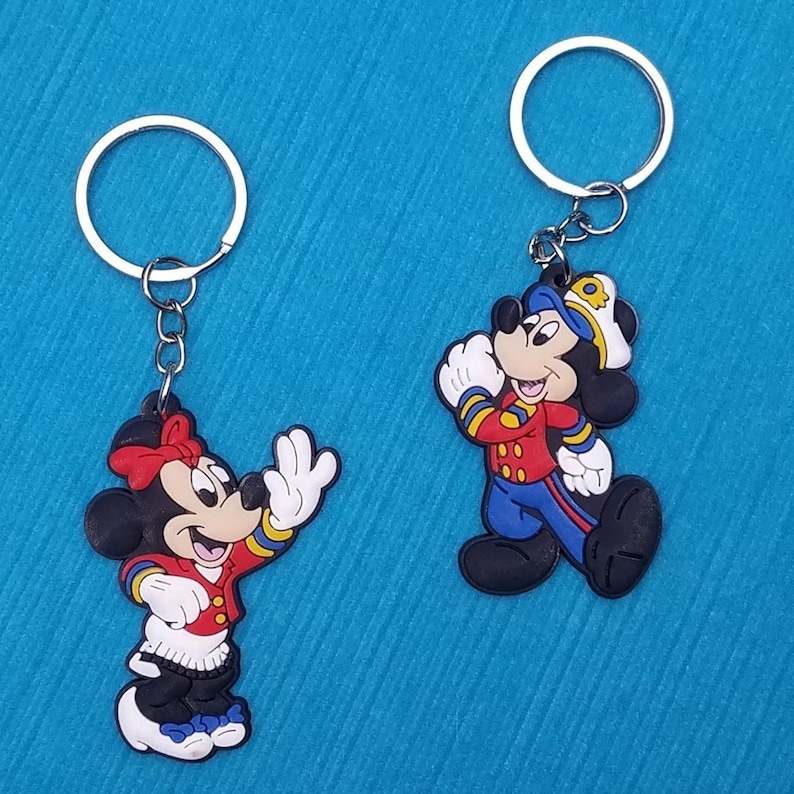 May include: Two keychains featuring Mickey Mouse and Minnie Mouse dressed in red and blue sailor outfits. The keychains are made of rubber and have silver key rings.