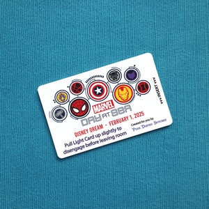 May include: A white card with a colorful Marvel Day at Sea logo featuring various Marvel characters. The card reads "Disney Dream - February 1, 2025" and "Pull Light Card up slightly to disengage before leaving room". The card also includes the text "Created for you by Pixie Dusted Stitches".