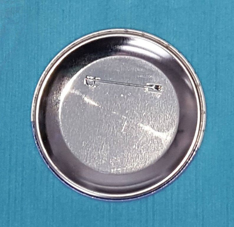 May include: The back of a silver metal button with a pin attached.