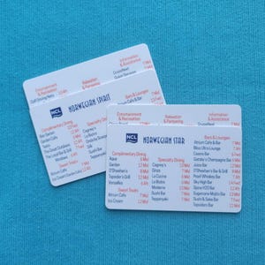 May include: Two white cards with the NCL logo and the words "Norwegian Spirit" and "Norwegian Star" printed on them. The cards list complimentary dining options, specialty dining options, bars and lounges, entertainment and recreation, relaxation and pampering, information and assistance, and guest services.