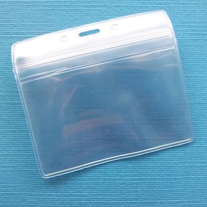 May include: A clear plastic badge holder with a hole at the top for a lanyard. The holder has a flap that closes with a zipper.