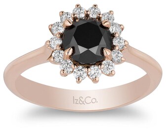 May include: A rose gold ring with a black diamond center stone surrounded by a halo of smaller white diamonds. The ring is engraved with the text "Iz&Co."