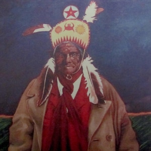 Op de afbeelding: Een portret van een indiaanse man die een traditionele hoofdtooi draagt met rode, witte en gele veren. Hij draagt een rood shirt en een bruine jas.