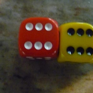 May include: Two dice, one red and one yellow, are shown. The red die displays six white dots, while the yellow die shows six black dots. The dice are positioned close together, suggesting a game or activity.