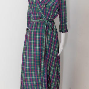 May include: A long, wrap-style dress in a plaid pattern of green, purple, and white. The dress features a V-neck, three-quarter sleeves, and a matching belt. The dress is displayed on a mannequin.