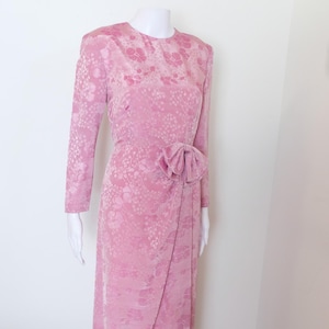 May include: A long pink dress with a floral pattern and a bow at the waist.