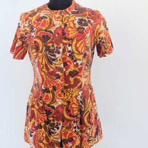 May include: A vintage short-sleeved top with a vibrant floral pattern in shades of red, yellow, brown, and white. The top features a mandarin collar and a button-down front. The garment is displayed on a mannequin against a plain white background.