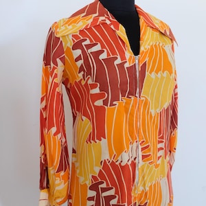 May include: A vintage zip-up shirt with a vibrant abstract pattern in shades of orange, yellow, and brown. The long-sleeved shirt features a collared neckline and a full-length zipper. The fabric has a flowing, lightweight appearance.