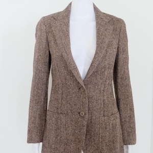 May include: Brown herringbone blazer with a notched lapel and two-button closure. The jacket features two front pockets and is displayed on a white mannequin. The blazer is a classic style, suitable for various occasions.