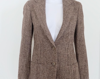 Op de afbeelding: Bruine visgraat blazer met een revers en sluiting met twee knopen. De jas heeft twee voorzakken en wordt gepresenteerd op een witte mannequin. Een klassieke stijl, geschikt voor diverse gelegenheden.
