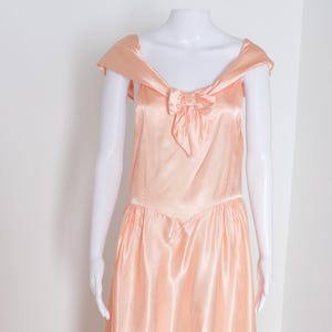 May include: A peach-colored satin dress with a bow at the neckline and cap sleeves.