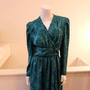 May include: A teal blue dress with a black abstract print. The dress has a V-neckline, long sleeves, and a fitted bodice. The skirt is gathered at the waist and falls to the knee.
