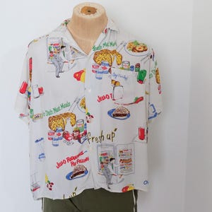 May include: White short-sleeved button-down shirt with a colorful food-themed print. The shirt features illustrations of various dishes, desserts, and beverages, with text including "Jello" and "fresh up".