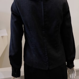 May include: A black long-sleeved blouse with a large, pointed collar and a zipper down the back. The blouse is made of a textured fabric and has a fitted silhouette.