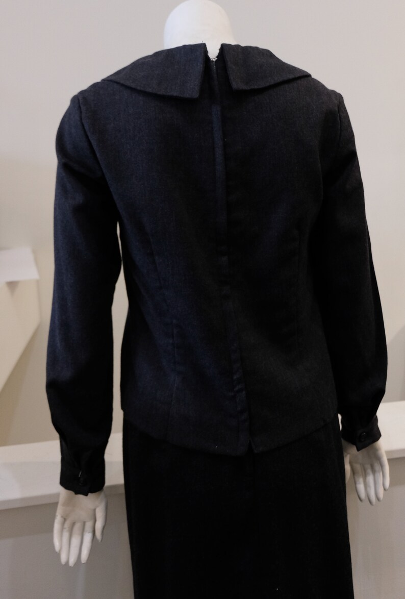 May include: A black long-sleeved blouse with a large, pointed collar and a zipper down the back. The blouse is made of a textured fabric and has a fitted silhouette.