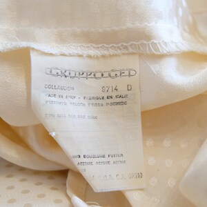 May include: A white tag with black text that reads "CKJPPOLGED", "COLLAUDOS", "9714 D", "FADE EL FRIQUE EN ITALIE", "PTESSUTO POLOTH TTISGO GEWEDE", "100% SUVA RM 02 00", "ING DOUBLURE FUTTER", "&Alpha;&Theta;&Epsilon;&Tau;&Alpha;&Tau;&Epsilon; &Lambda;&Omicron;&Upsilon;&Tau;&Alpha;ATE ACESAR", "DA CA. 07510".