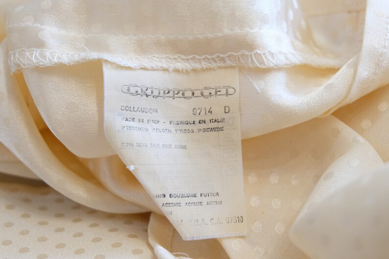 May include: A white tag with black text that reads "CKJPPOLGED", "COLLAUDOS", "9714 D", "FADE EL FRIQUE EN ITALIE", "PTESSUTO POLOTH TTISGO GEWEDE", "100% SUVA RM 02 00", "ING DOUBLURE FUTTER", "&Alpha;&Theta;&Epsilon;&Tau;&Alpha;&Tau;&Epsilon; &Lambda;&Omicron;&Upsilon;&Tau;&Alpha;ATE ACESAR", "DA CA. 07510".