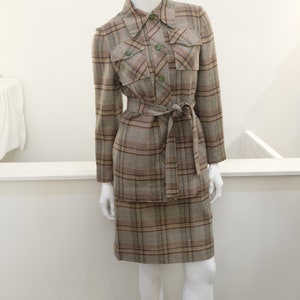 May include: A brown and beige plaid skirt suit with a long-sleeved jacket and a matching skirt. The jacket has a collared neckline, a button closure, and two flap pockets. The skirt has a high waist and a straight silhouette.