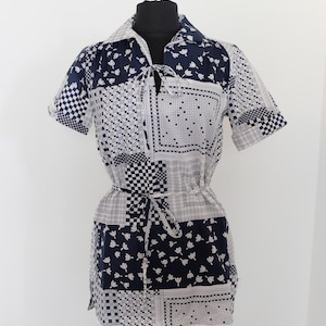 May include: A vintage patchwork dress in navy blue and white, displayed on a mannequin. The dress features a collared neckline, short sleeves, and a tie at the waist. The fabric is patterned with geometric and floral designs.