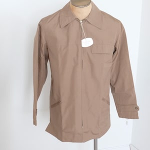 May include: A light brown jacket featuring a pointed collar, a full-length front zipper, long sleeves with buttoned cuffs, and a small chest pocket. A white rectangular tag is attached to the zipper pull near the neckline of the garment.