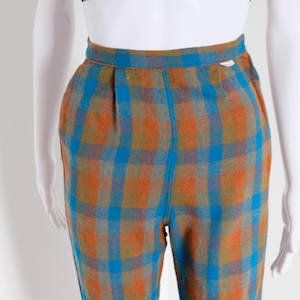 May include: Trousers with a plaid pattern in shades of orange, blue, and brown. The high-waisted pants are displayed on a mannequin. The plaid design features a grid of intersecting lines, creating a classic and timeless look. The trousers are made of a woven fabric.